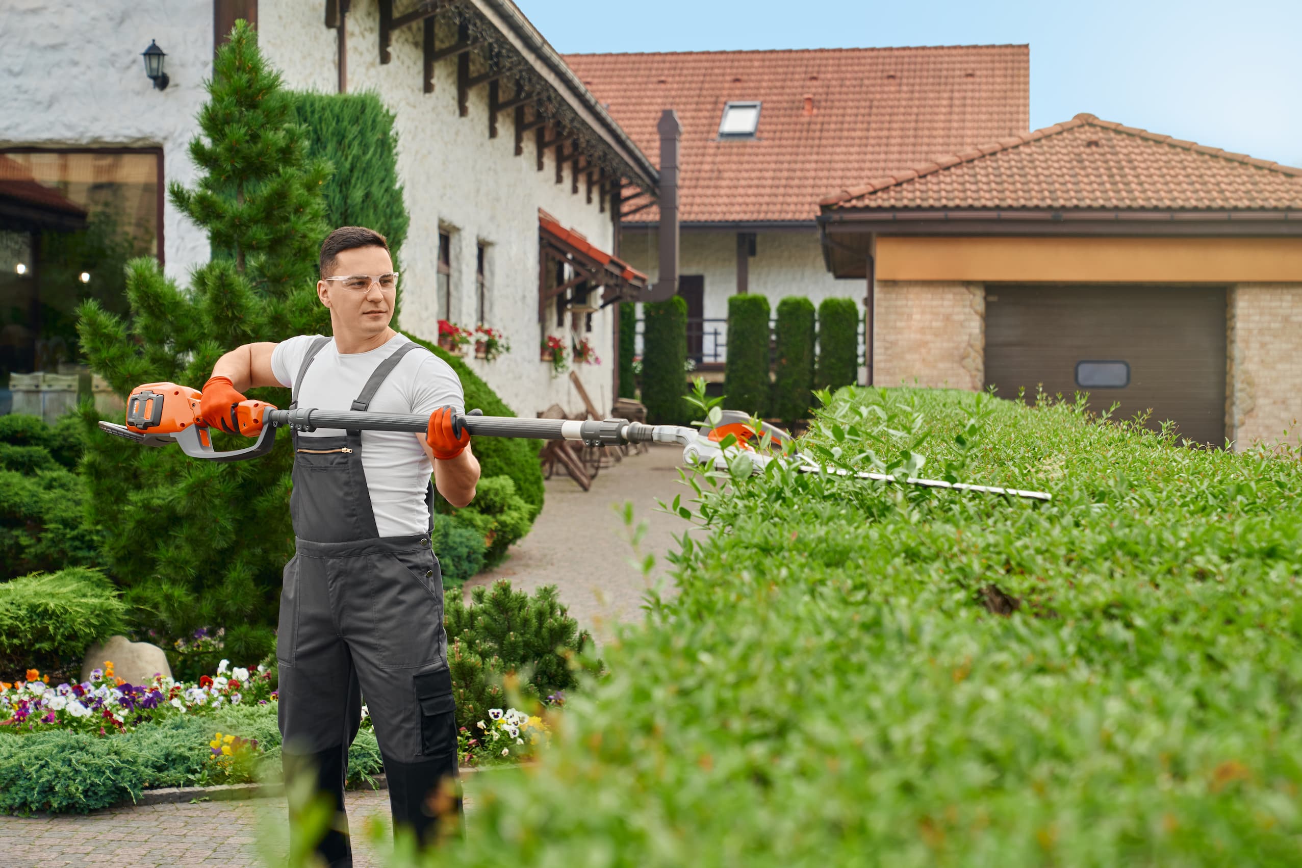 A landscaper trimming hedges outside a home