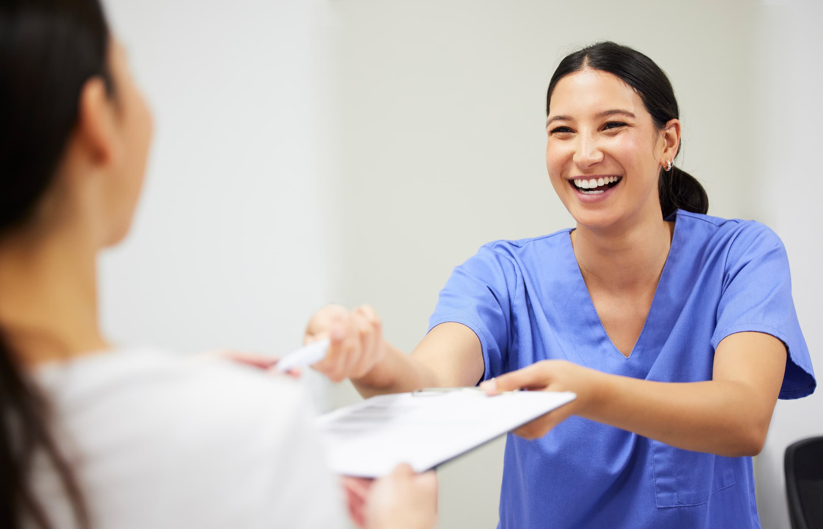 A healthcare worker in scrubs handing paperwork to a patient